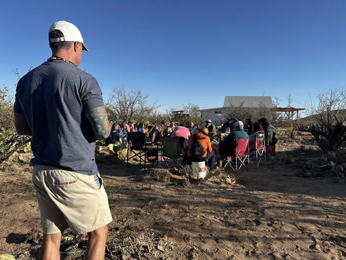 A facilitator speaking to veterans seated in an outdoor circle at dusk